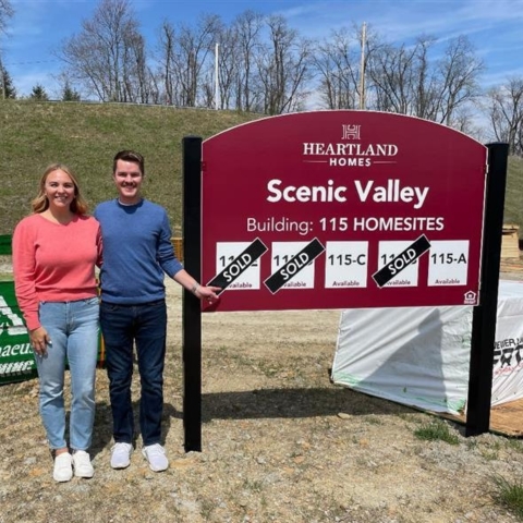 Smiling couple standing in front of Heartland Homes Scenic Valley sign