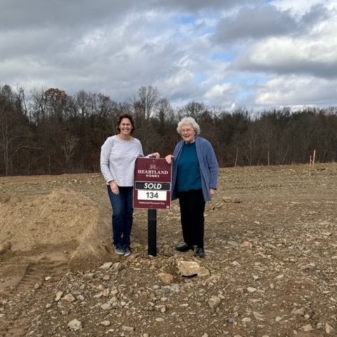 Family standing on rocky lot at Heartland Homes site marked 'SOLD'