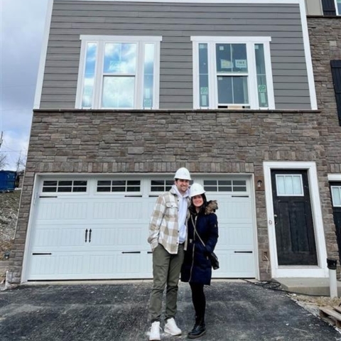 Couple in hard hats standing in front of newly built two-story Heartland Homes house with stone facade