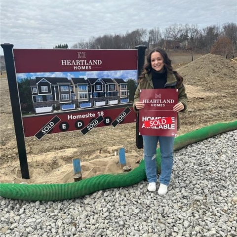 Individual standing on gravel path at Heartland Homes construction site – holding 'Home Sold' sign