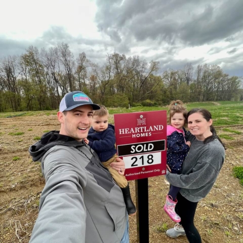 Family celebrating new home lot purchase with 'SOLD' Heartland Homes sign
