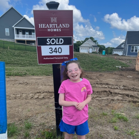 Smiling child in front of Heartland Homes 'SOLD' sign